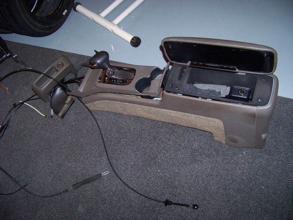 Car's center console removed, showing the shifter, cup holders, and open storage compartment