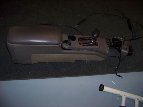 1999 Mercury Grand Marquis - A disassembled car center console unit with a chrome gear shifter is shown.