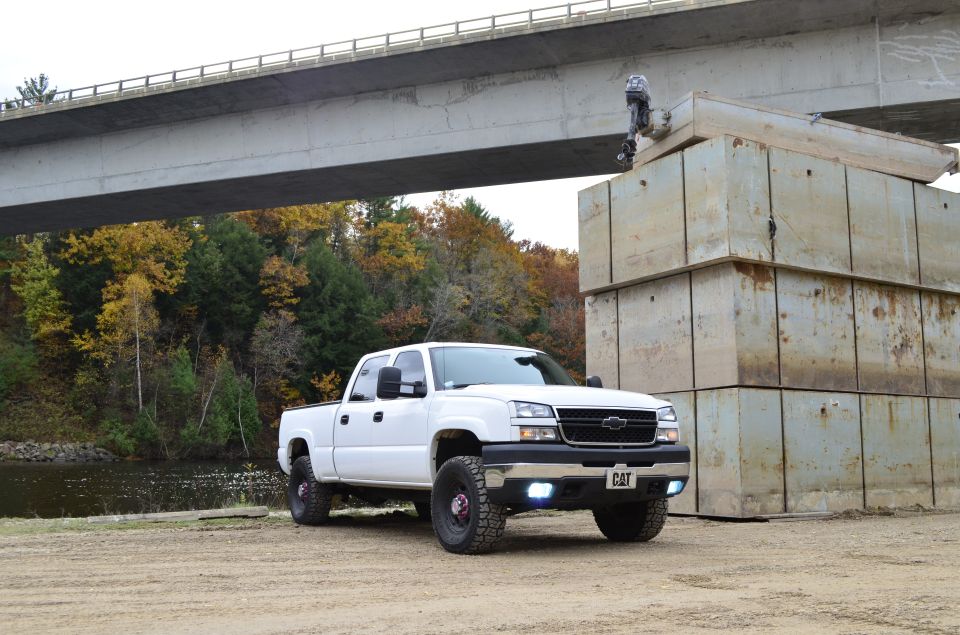 White Chevrolet pickup truck with a CAT emblem on the front grille, parked outdoors under a concrete bridge
