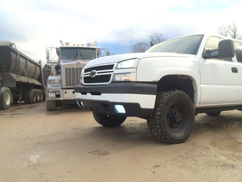 2006 Chevrolet Silverado 2500 - A white 2006 Chevrolet Silverado 2500 pickup truck is parked in front of a large semi-truck.