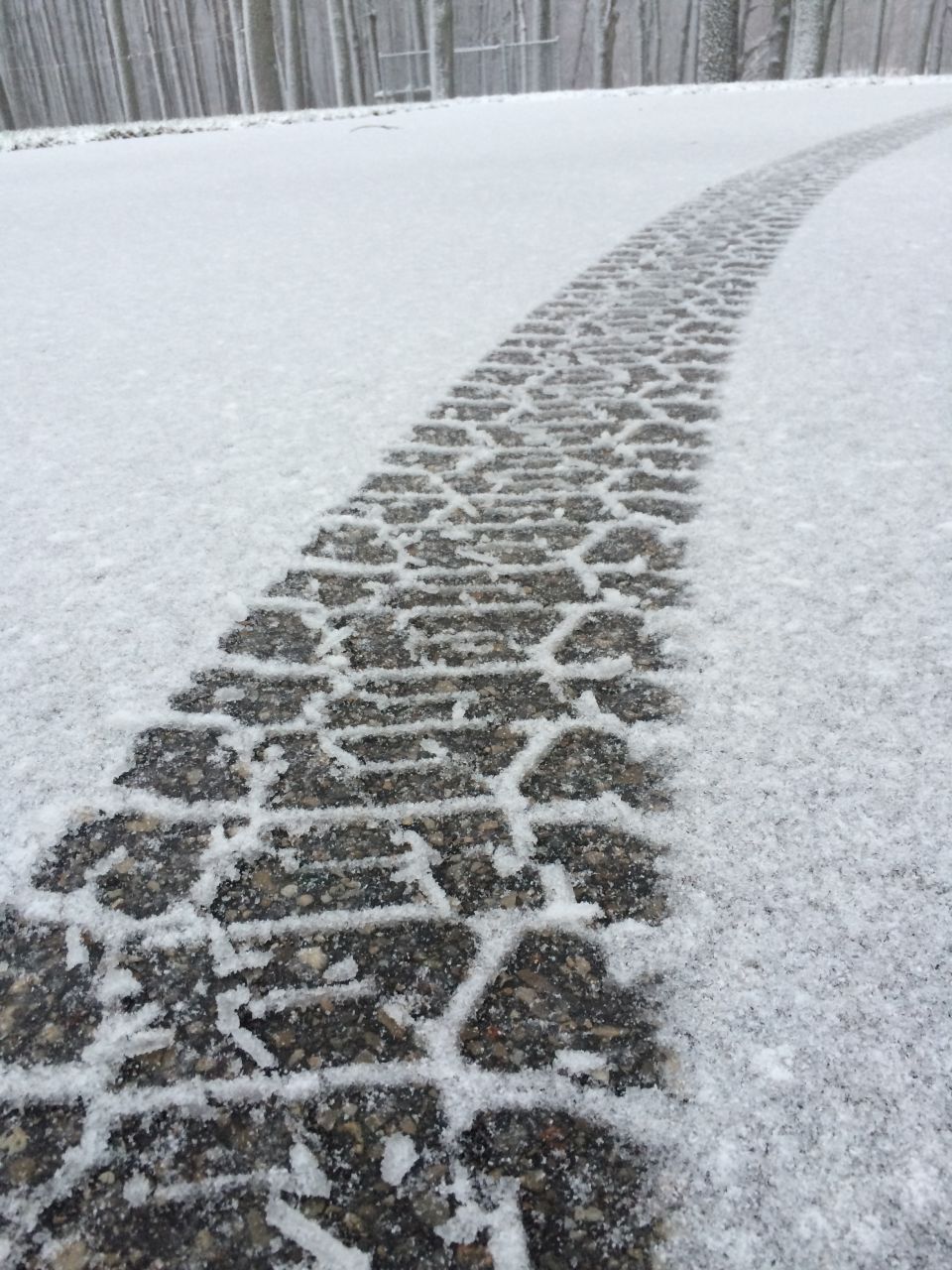 Tire track in snow on a road with trees in the background