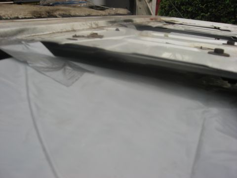 1994 Ford Bronco - Close-up of a white car tailgate, revealing exposed metal and plastic sheeting, indicating repair or disassembly.