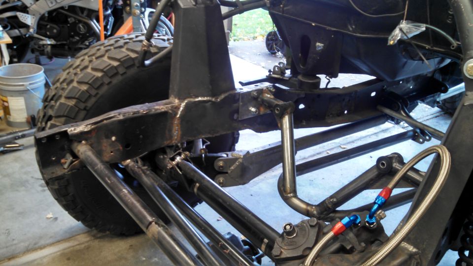 Close-up of a custom off-road vehicle's suspension and frame, showing heavy-duty components and braided hoses