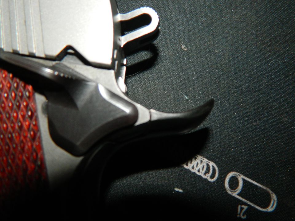Close-up of a pistol's grip and slide, showing textured red grip panels and metallic slide
