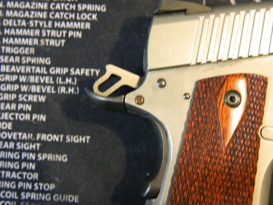 Close-up of a pistol's grip safety and checkered wood grip against a parts list