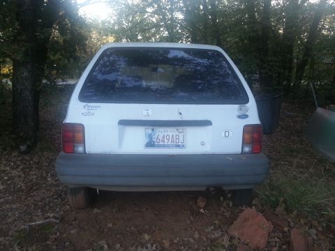 1991 Ford Festiva - The rear of a white hatchback is shown parked outdoors with trees in the background.