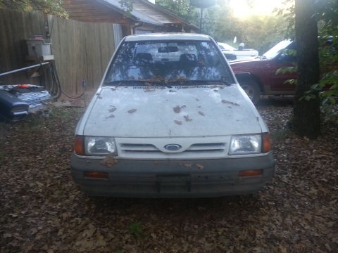 1991 Ford Festiva - Front view of a white 1991 Ford Festiva parked outside with leaves scattered on its hood.