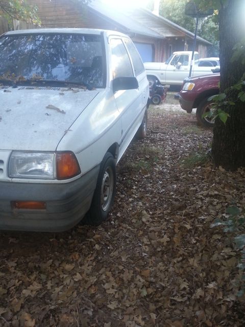 1991 Ford Festiva - A white 1991 Ford Festiva is parked next to other vehicles in a yard.