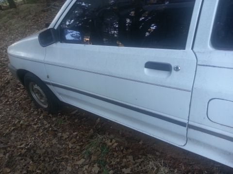 1991 Ford Festiva - The side profile of a white 1991 Ford Festiva shows its door and fender details.