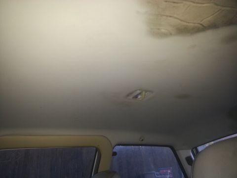 1991 Ford Festiva - The headliner of a car interior shows signs of wear and tear, including stains and a damaged light fixture.
