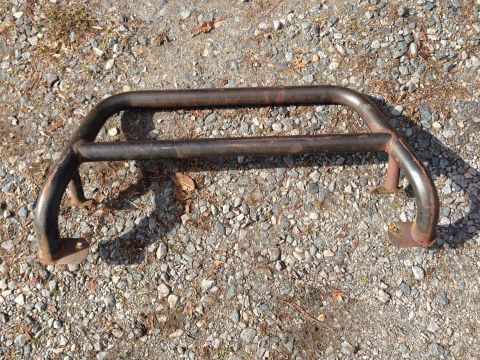 1979 Ford Bronco - A rusty metal bull bar lies on a gravel surface with some fallen leaves.