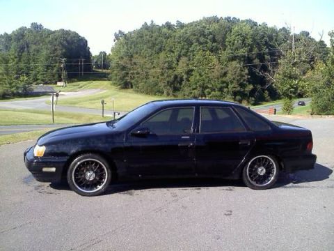 1993 Ford Taurus - Side profile of a black 1993 Ford Taurus sedan with custom wheels parked outdoors.