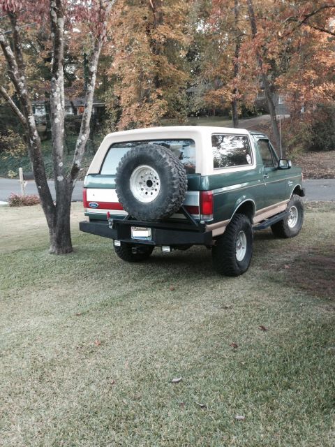 1989 Ford Bronco - A green and tan Ford Bronco is parked on a grassy lawn with trees in the background.