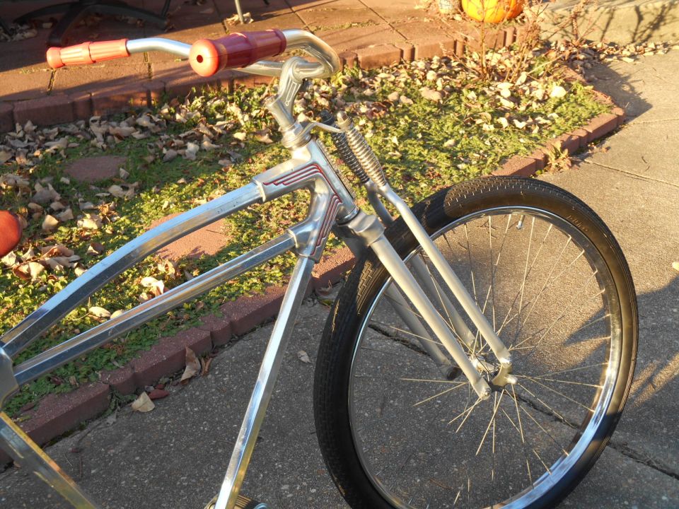 Chrome bicycle frame with red grips and a spoked wheel
