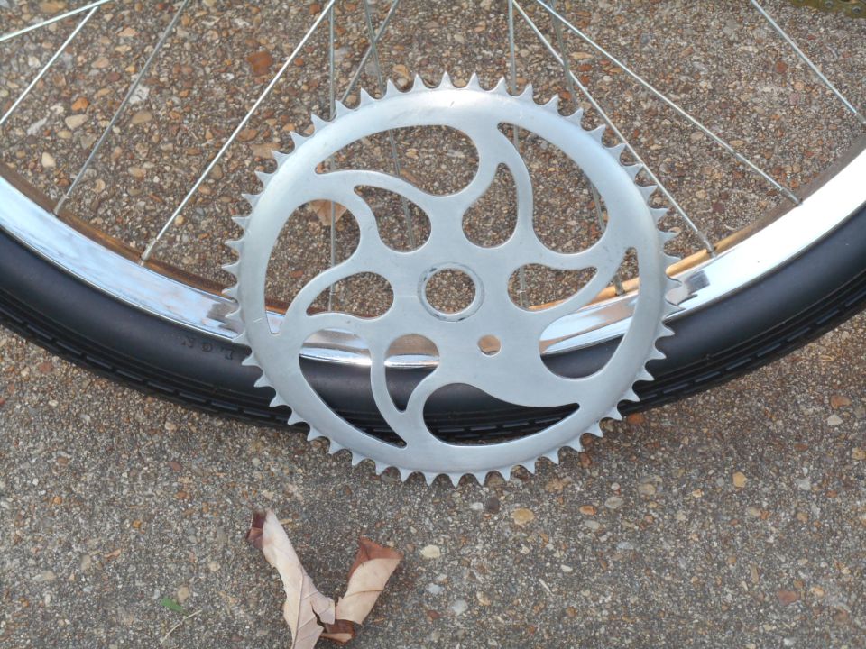 Silver bicycle chainring with intricate cutouts next to a tire and spokes