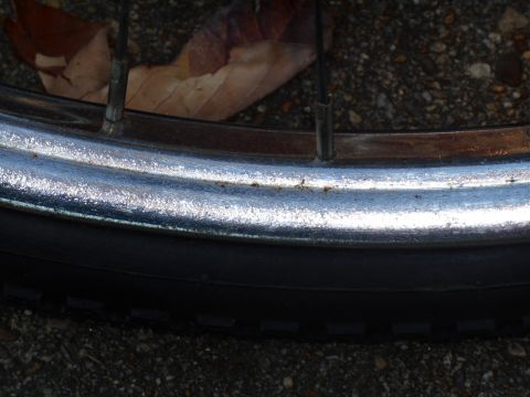 Close-up of a bicycle wheel rim and tire with spokes and a fallen leaf