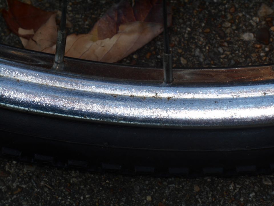 Close-up of a bicycle wheel rim and tire with spokes and a fallen leaf