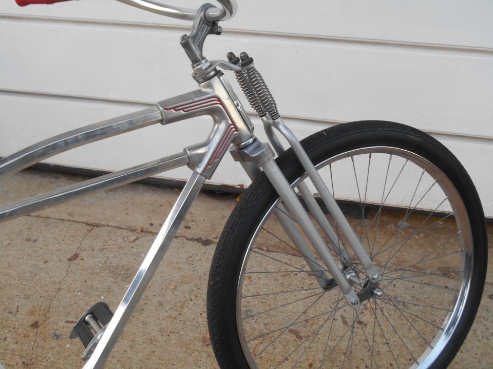 Close-up of a vintage bicycle's front fork and wheel. It has a chrome frame and red handlebars