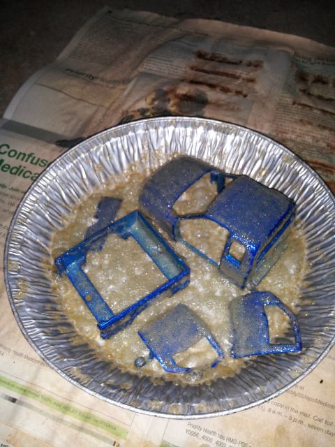 1995 Ford Bronco - Model car body parts are submerged in a cleaning solution within a foil pan, resting on newspaper.
