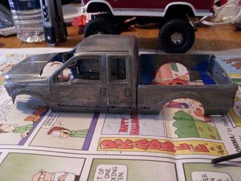 1995 Ford Bronco - Unfinished model truck body sits on a surface covered with comic strips. Another model vehicle is partially visible in the background.