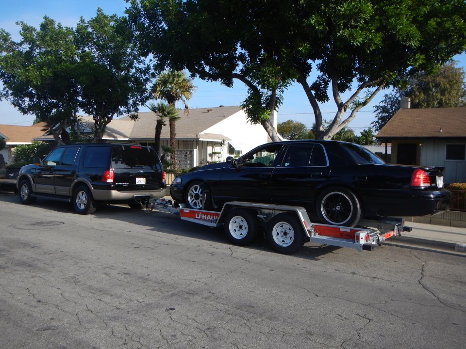 Black SUV towing a black Ford sedan on a U-Haul trailer on a street