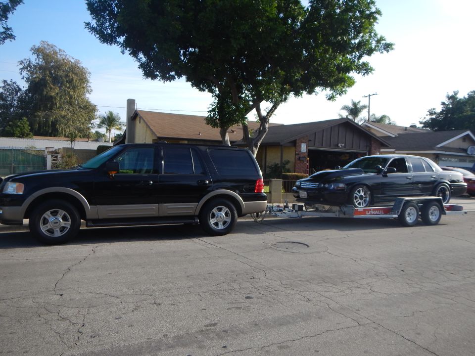 Black Ford Expedition towing a sedan on a U-Haul trailer curbside