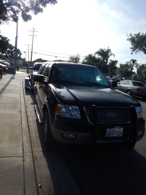 2003 Ford Crown Victoria - Black Ford Expedition with front brush guard and plate 4XTF376 parked at a curb, backlit by bright sun.