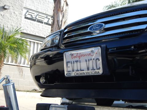 2003 Ford Crown Victoria - Close view of a black Ford sedan's front bumper with a California plate reading EVIL VIC in a Crown Victoria frame below the Ford grille.