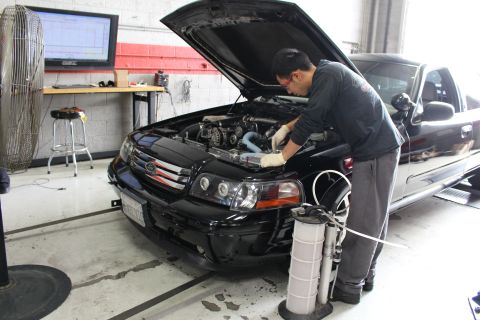 2003 Ford Crown Victoria - mechanic leans into the engine bay of a black Ford sedan with its hood raised inside a tuning shop, a coolant tool beside the bumper.