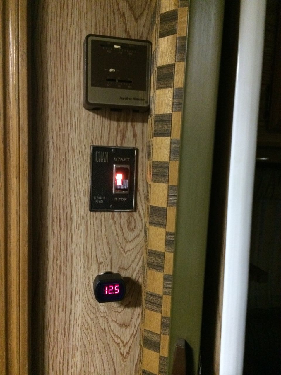 RV interior panel with a thermostat, a start/stop switch, and a digital voltage meter showing 12.5