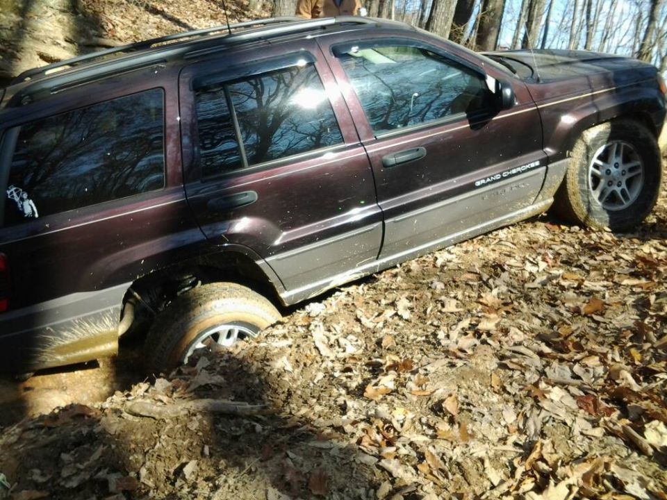 Jeep Grand Cherokee stuck in mud on a wooded trail. The front right wheel is buried
