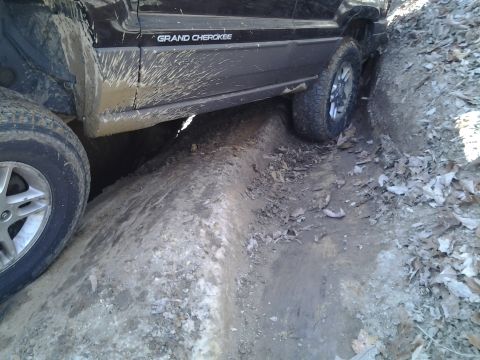 1995 Ford Bronco - A black Jeep Grand Cherokee navigates a difficult muddy terrain, with its side and wheels clearly visible.