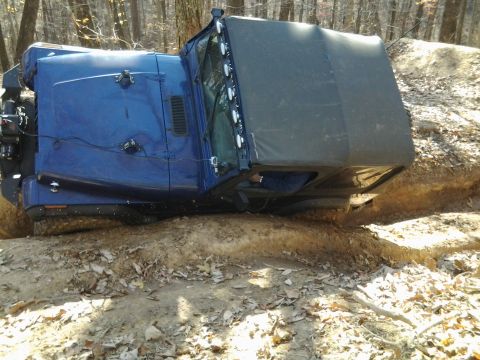 1995 Ford Bronco - This blue off-road vehicle appears to be stuck on its side in a muddy ditch during an off-road excursion.