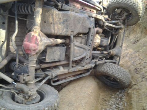 1995 Ford Bronco - This vehicle has rolled onto its side, revealing its undercarriage and suspension components in a dirt terrain.