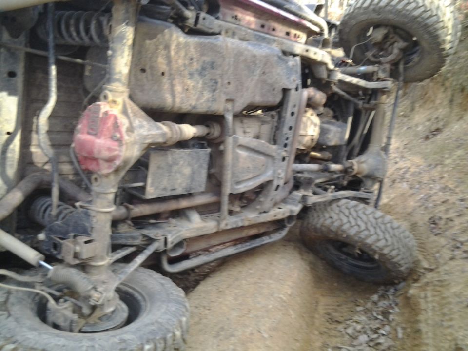 Off-road vehicle flipped onto its side in dirt, showing undercarriage and suspension. Supermotors.net logo visible