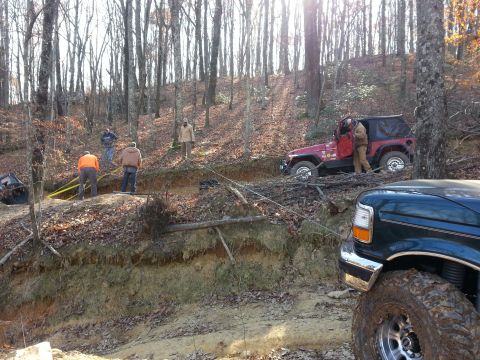 1995 Ford Bronco - Off-road recovery scene with a Jeep stuck and a truck assisting in a wooded area.