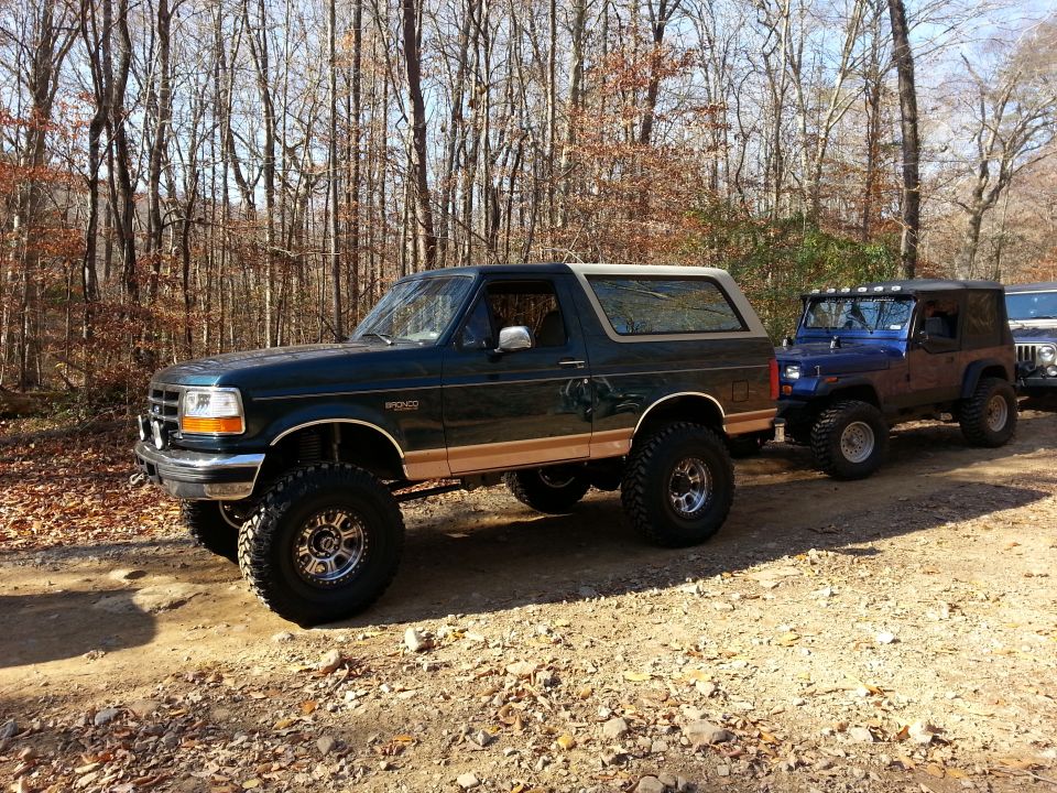Dark green 1995 Ford Bronco with tan trim and lifted suspension parked on a dirt road
