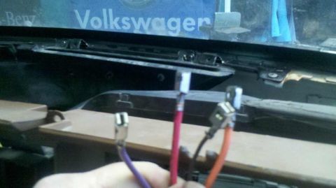 1982 Ford Bronco - Close-up of exposed wiring harnesses with metal connectors inside a vehicle's dashboard area. A partial view of the windshield shows text t…