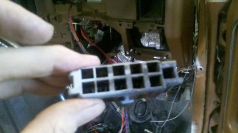 1982 Ford Bronco - A hand holds a gray electrical connector with multiple square openings, revealing a tangle of wires and vehicle components in the backgroun…