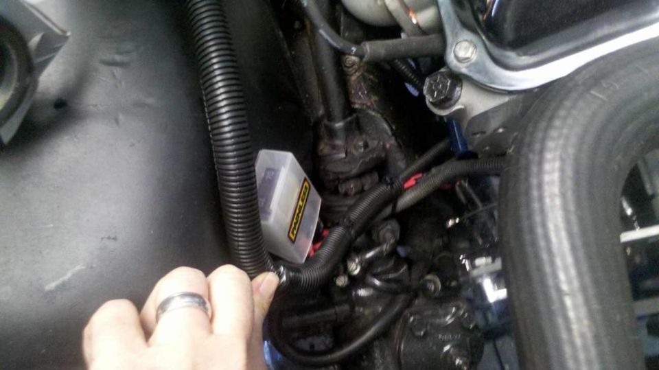 Close-up of a hand pointing to a fuse box in a vehicle engine bay.