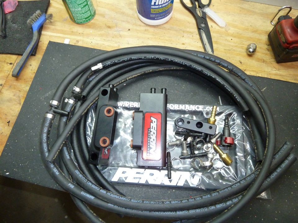 Black fuel lines and Perrin Performance parts on a workbench.