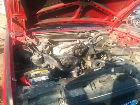 1988 Ford Bronco - The open red hood of a Ford truck reveals the engine bay, with a battery visible in the foreground.