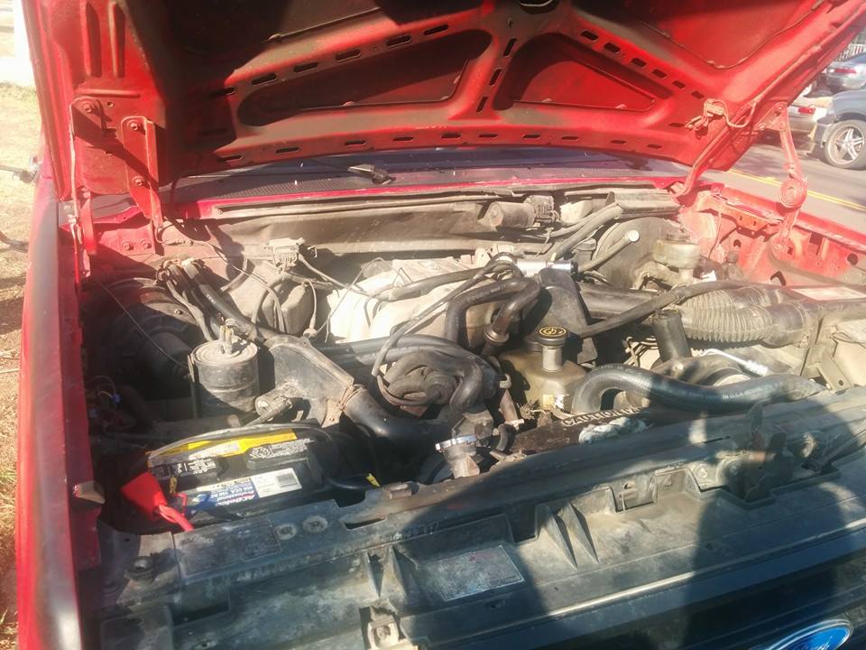 Close-up of a red Ford truck engine bay with the hood open.