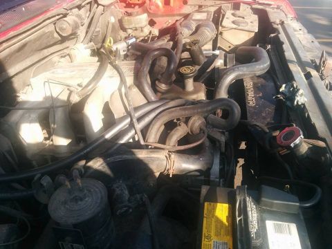 1988 Ford Bronco - A close-up, overhead view of the engine bay of a red Ford Bronco, focusing on the engine components, hoses, and battery.