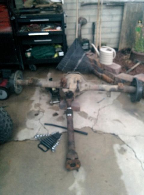 1988 Ford Bronco - A disassembled rear axle assembly and driveshaft are laid out on a concrete floor, likely in a garage or driveway. Tools, including a set o…