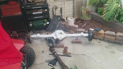 1988 Ford Bronco - A rear differential assembly, painted white, is supported by jack stands and blocks on a concrete driveway. Tools and a driveshaft are scat…