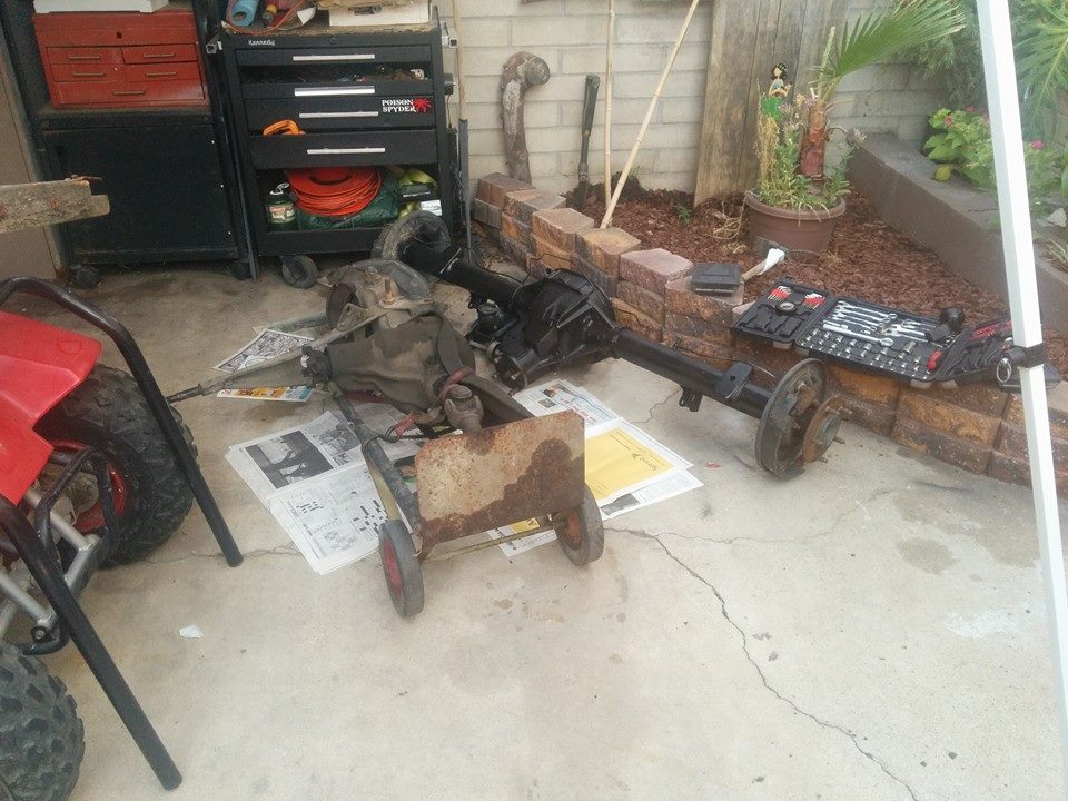Two vehicle rear axle assemblies on the ground next to a red ATV, with tools in the background.