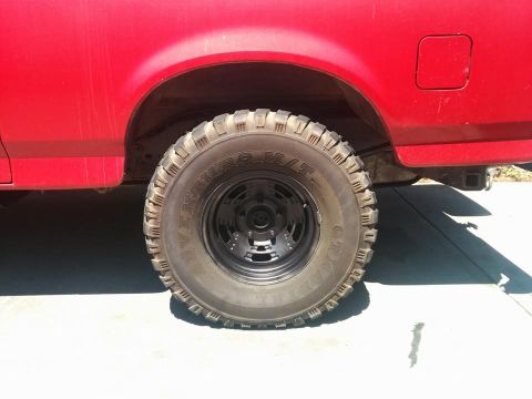 1988 Ford Bronco - A close-up side view of the rear tire and fender of a red Ford Bronco. The tire is a large, aggressive tread all-terrain tire with a black…