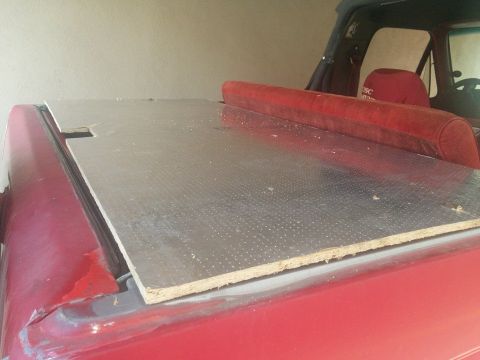 1988 Ford Bronco - A custom-made wooden bed cover with a metallic finish is installed on the bed of a red pickup truck. The cover has a cutout for a raised re…