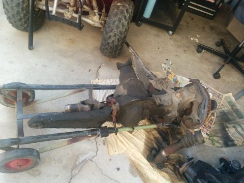 1988 Ford Bronco - A disassembled front axle assembly, likely from a 1988 Ford Bronco, is resting on a dolly and on the ground. The assembly includes a differ…